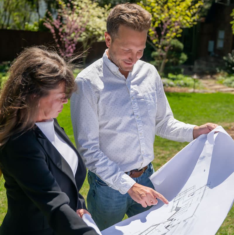 Two professionals reviewing architectural drawings outdoors on a sunny day.